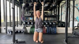 A woman suspended from a gym ring, working to banish upper body pain.
