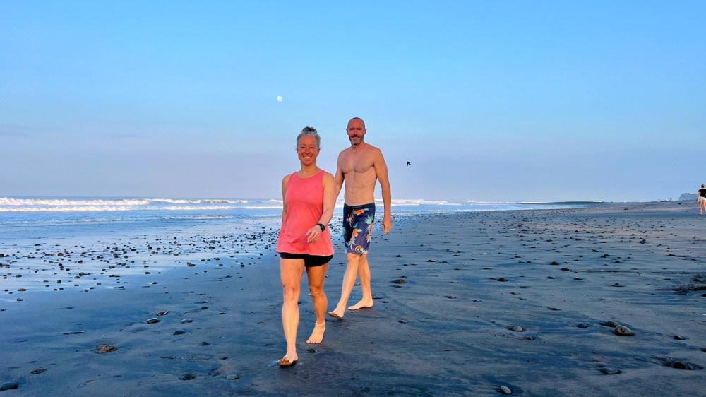 A couple strolling barefoot, along the sandy beach with the ocean waves in the background.