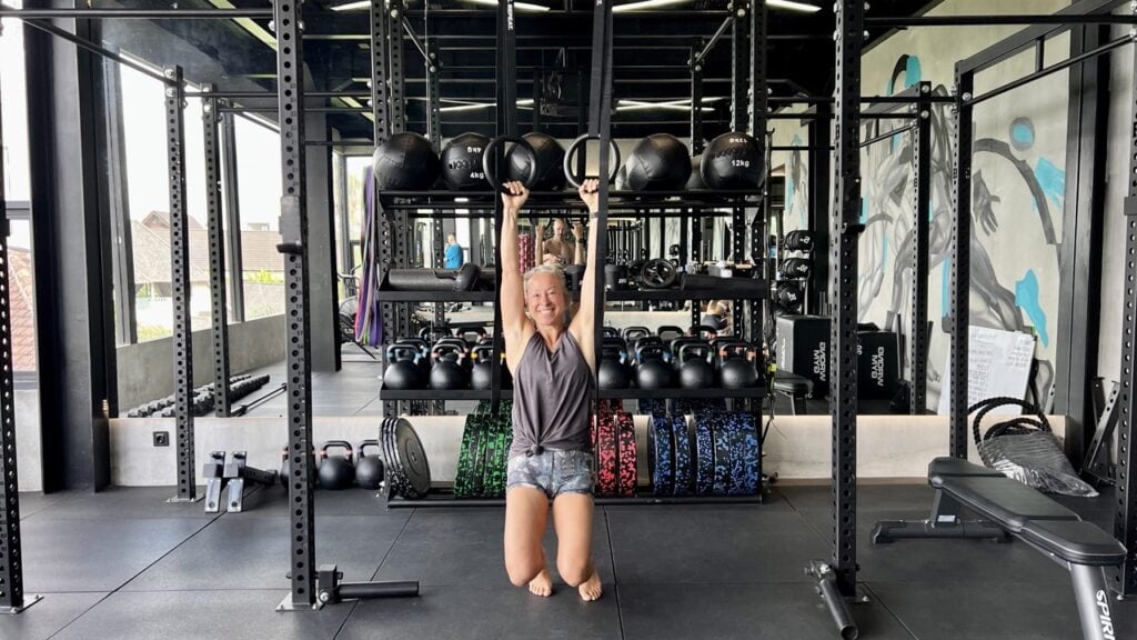 A woman suspended from a gym ring, working to enhance her upper body strength.