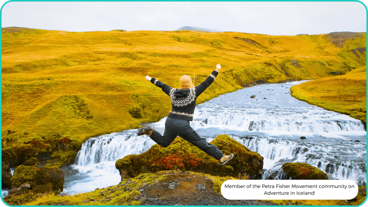 A member of the community jumping for joy in front of a flowing river in green Iceland.