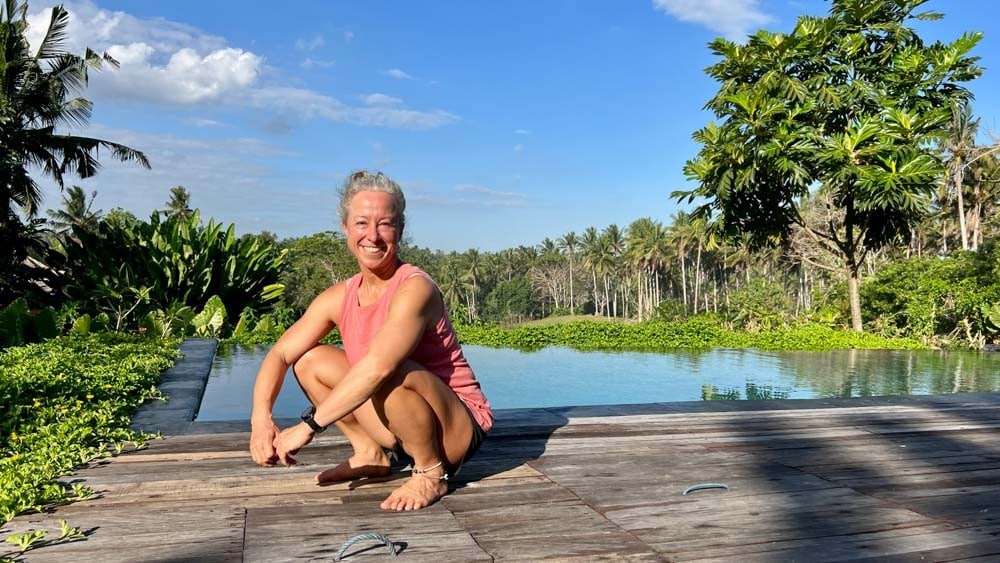 A joyful woman squatting by a pool.