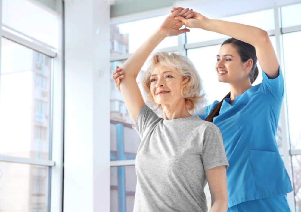 Physiotherapist providing shoulder treatment to a content elderly woman, enjoying the session for pain relief.