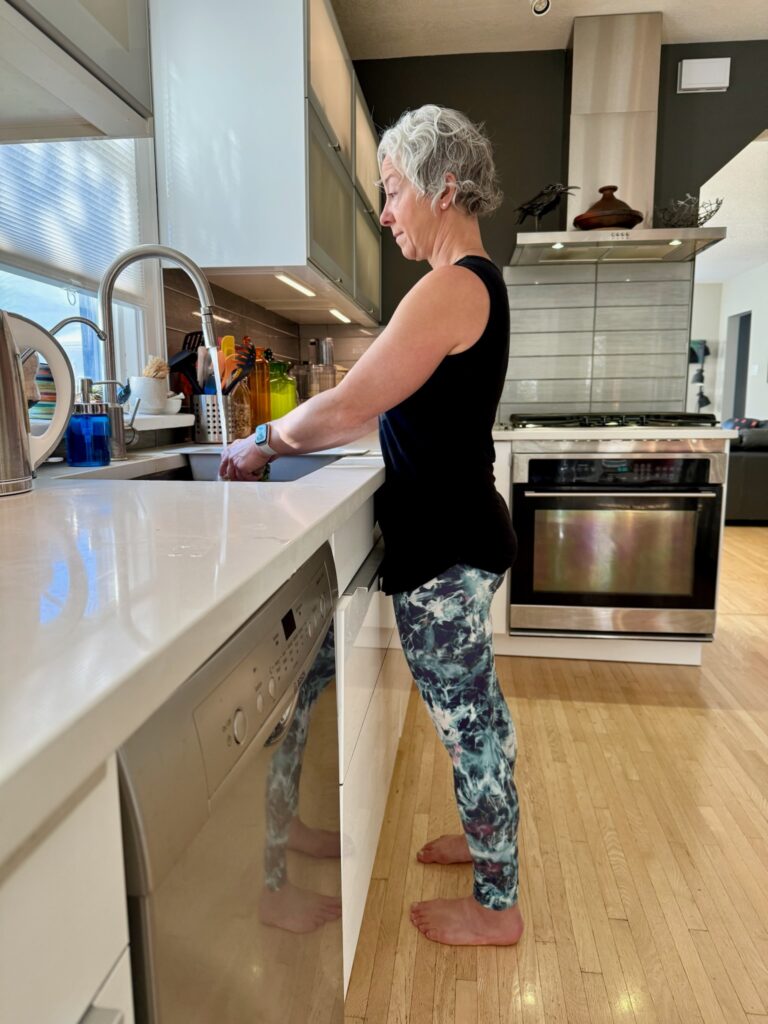 Woman washing dishes barefoot in a modern kitchen.